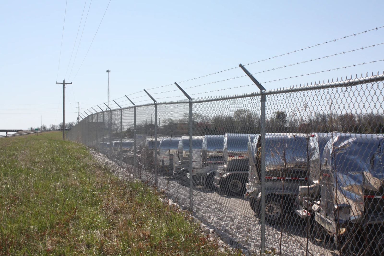 A row of cars are parked behind a barbed wire fence.
