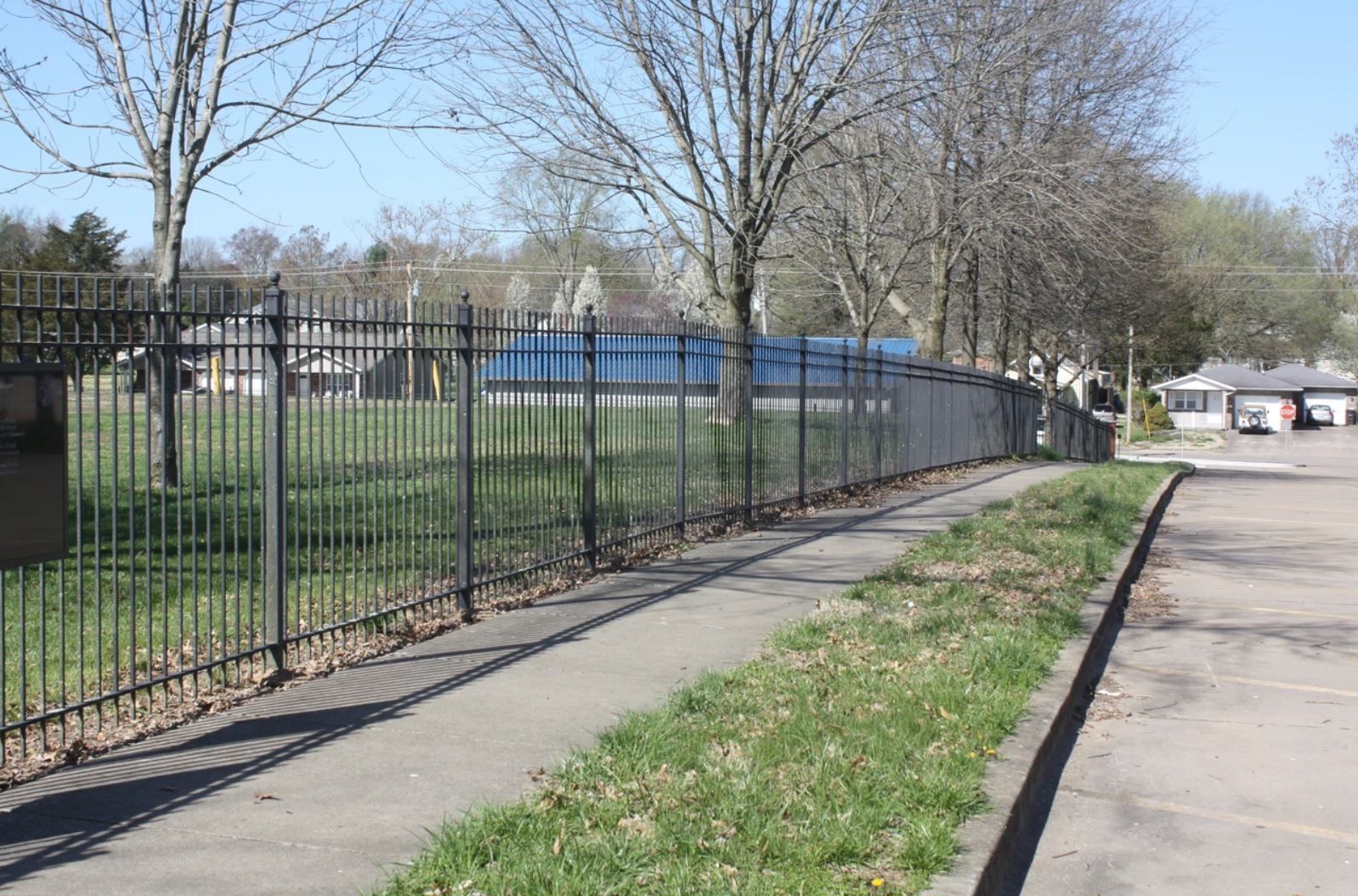 A metal fence along a sidewalk with trees in the background.
