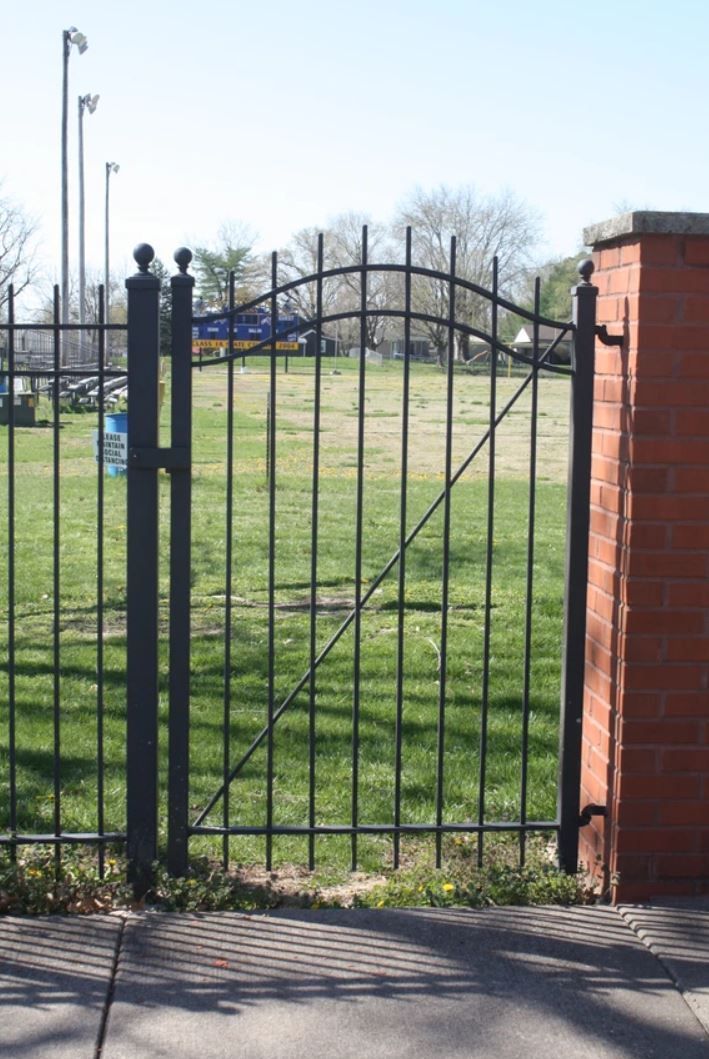 A wrought iron gate is open to a grassy field