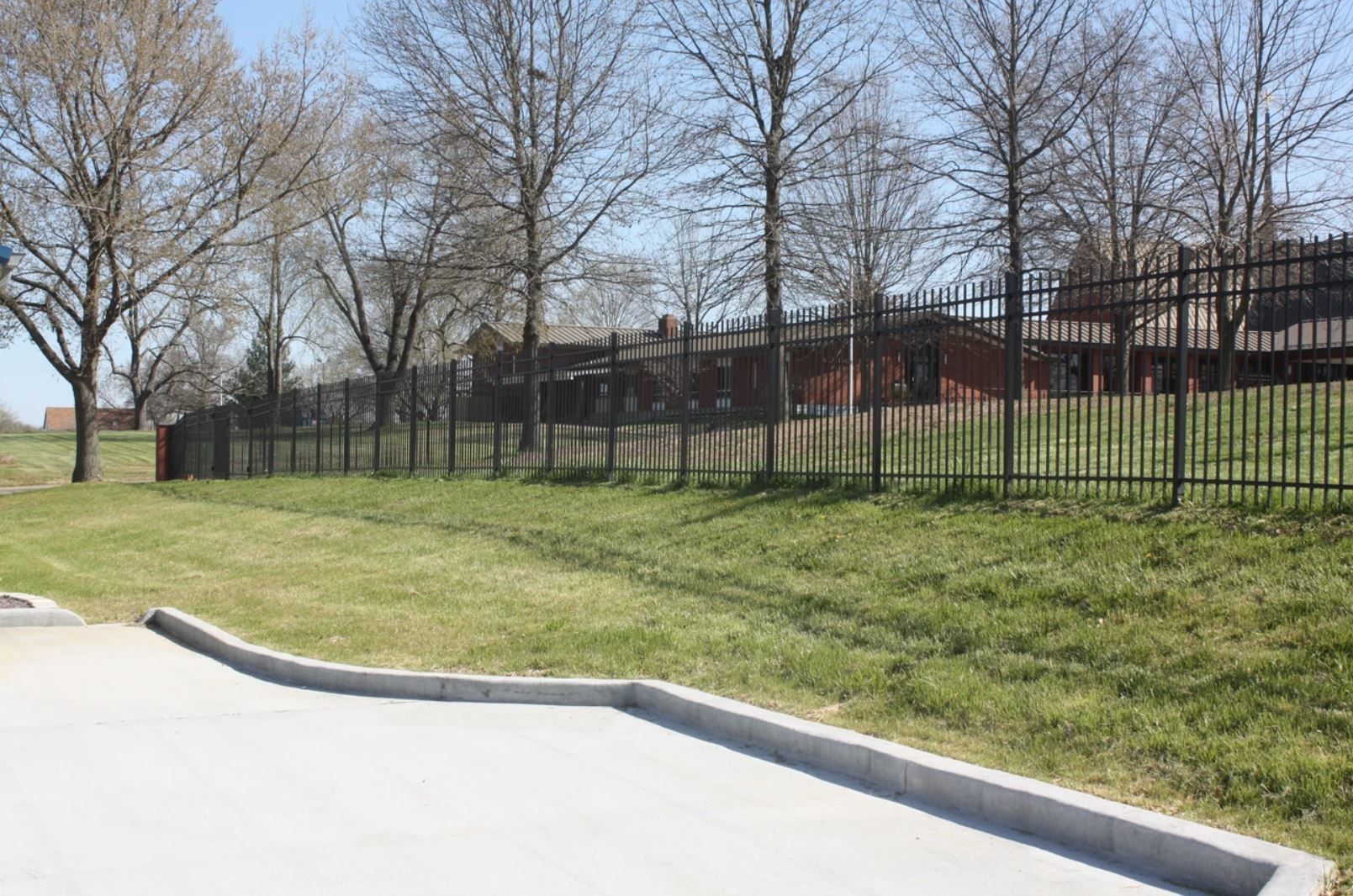 A fence surrounds a grassy field with trees in the background.