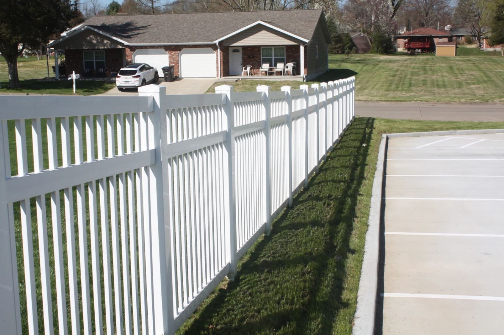 A white fence surrounds a driveway in front of a house