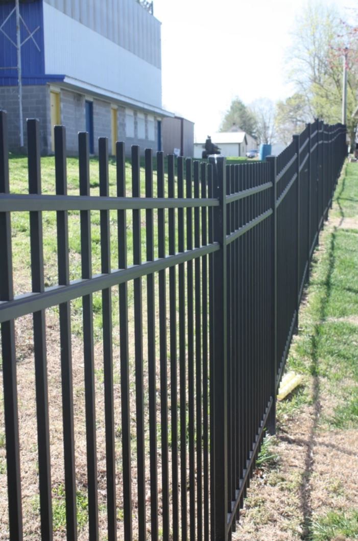 A black metal fence surrounds a grassy field in front of a building.