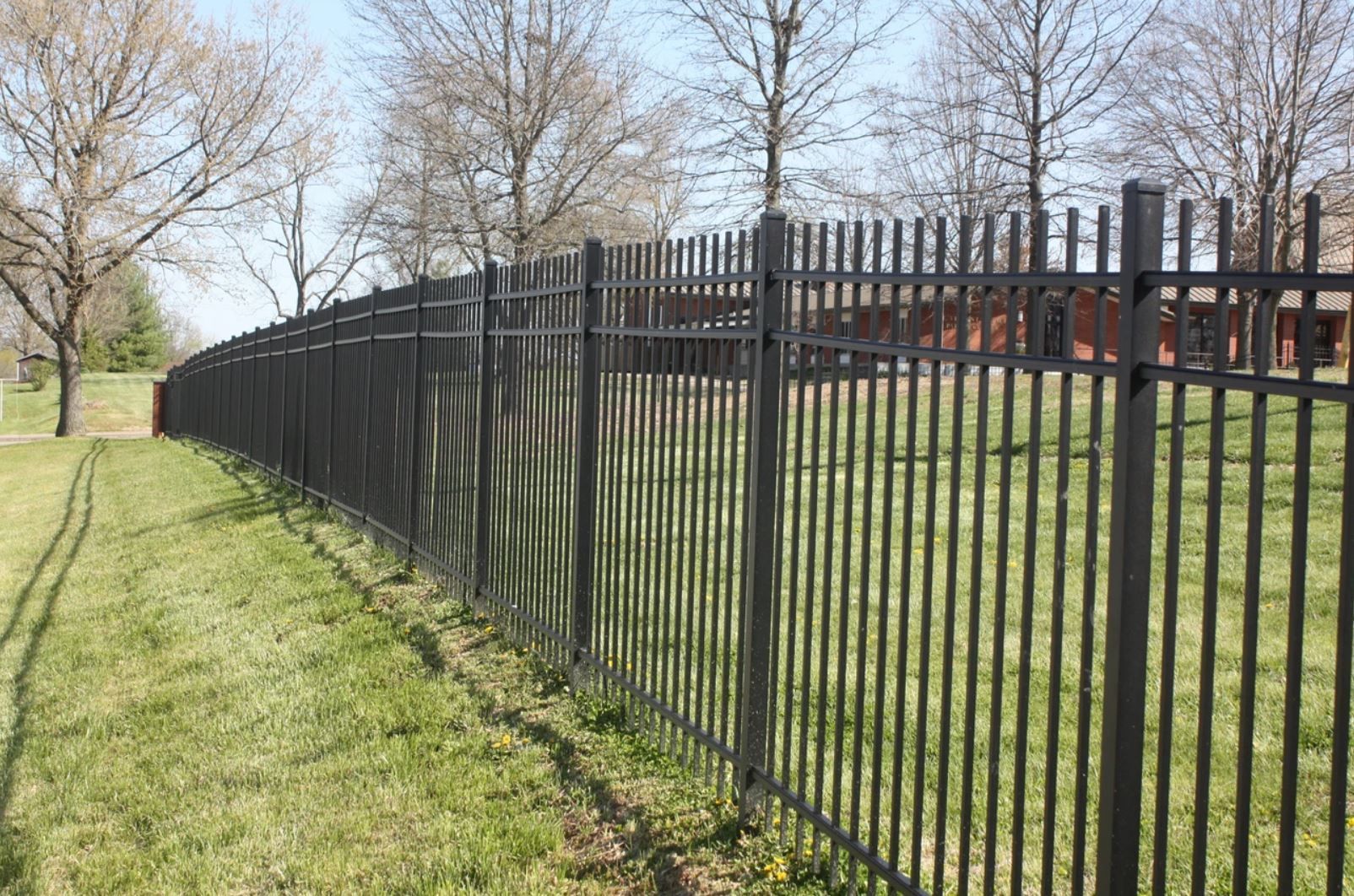 A black metal fence surrounds a lush green field.
