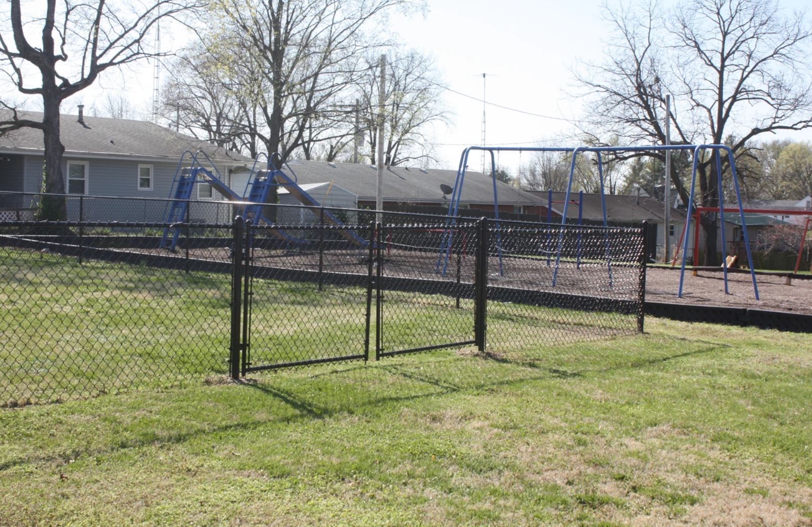 A playground with swings and a fence in front of a house.
