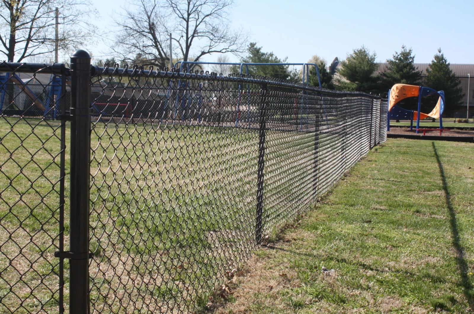 A chain link fence surrounds a playground in a park