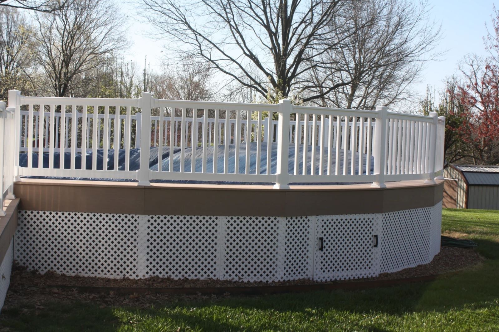 A white fence surrounds a swimming pool with trees in the background