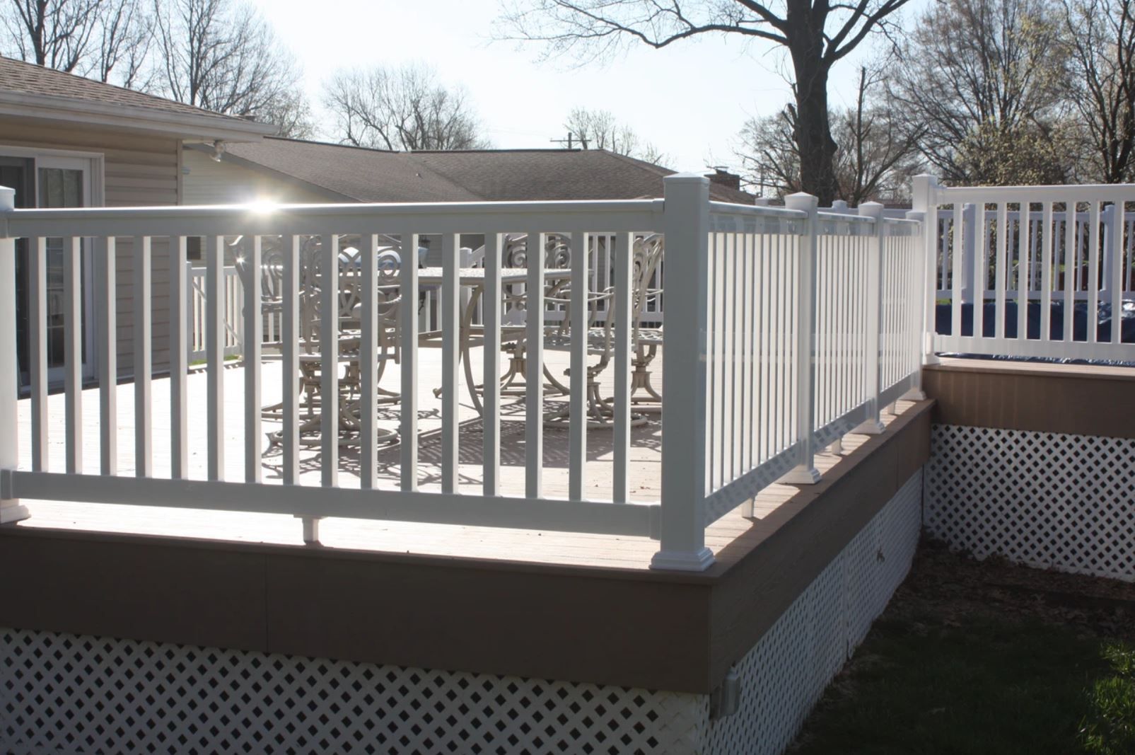 A deck with a white railing and a house in the background