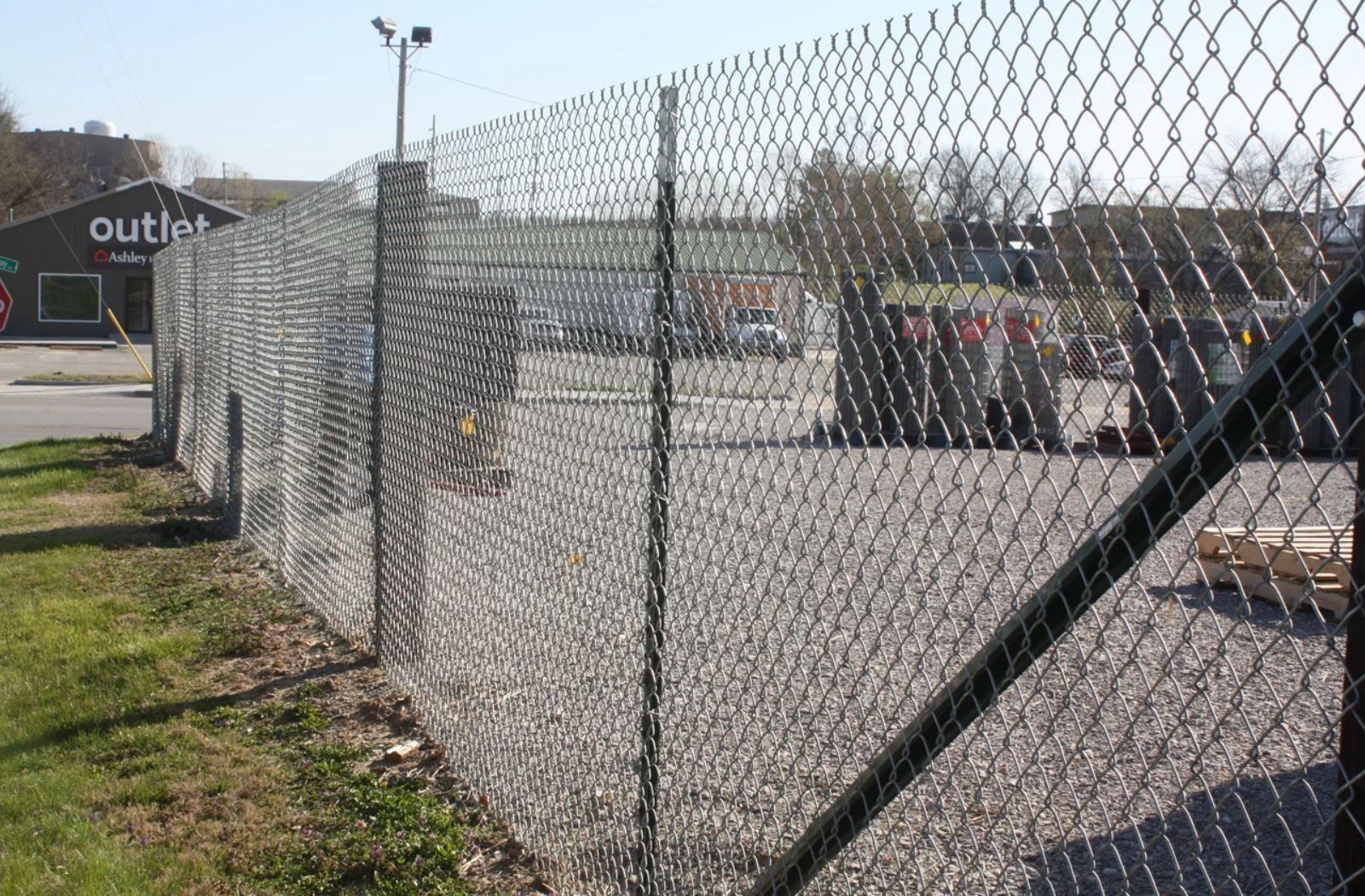 A chain link fence surrounds a parking lot in front of an outlet store.