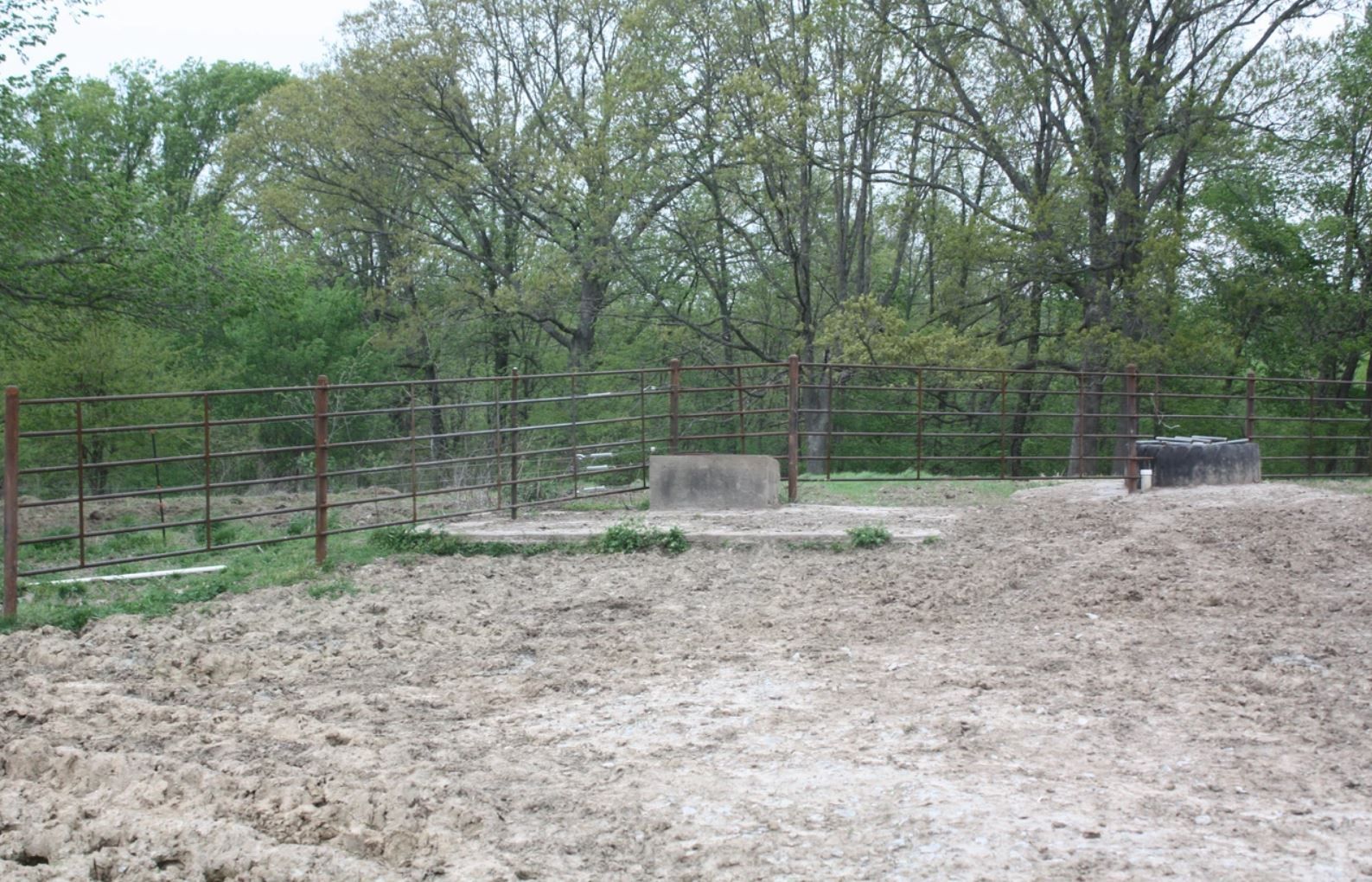 A dirt field with a fence and trees in the background.