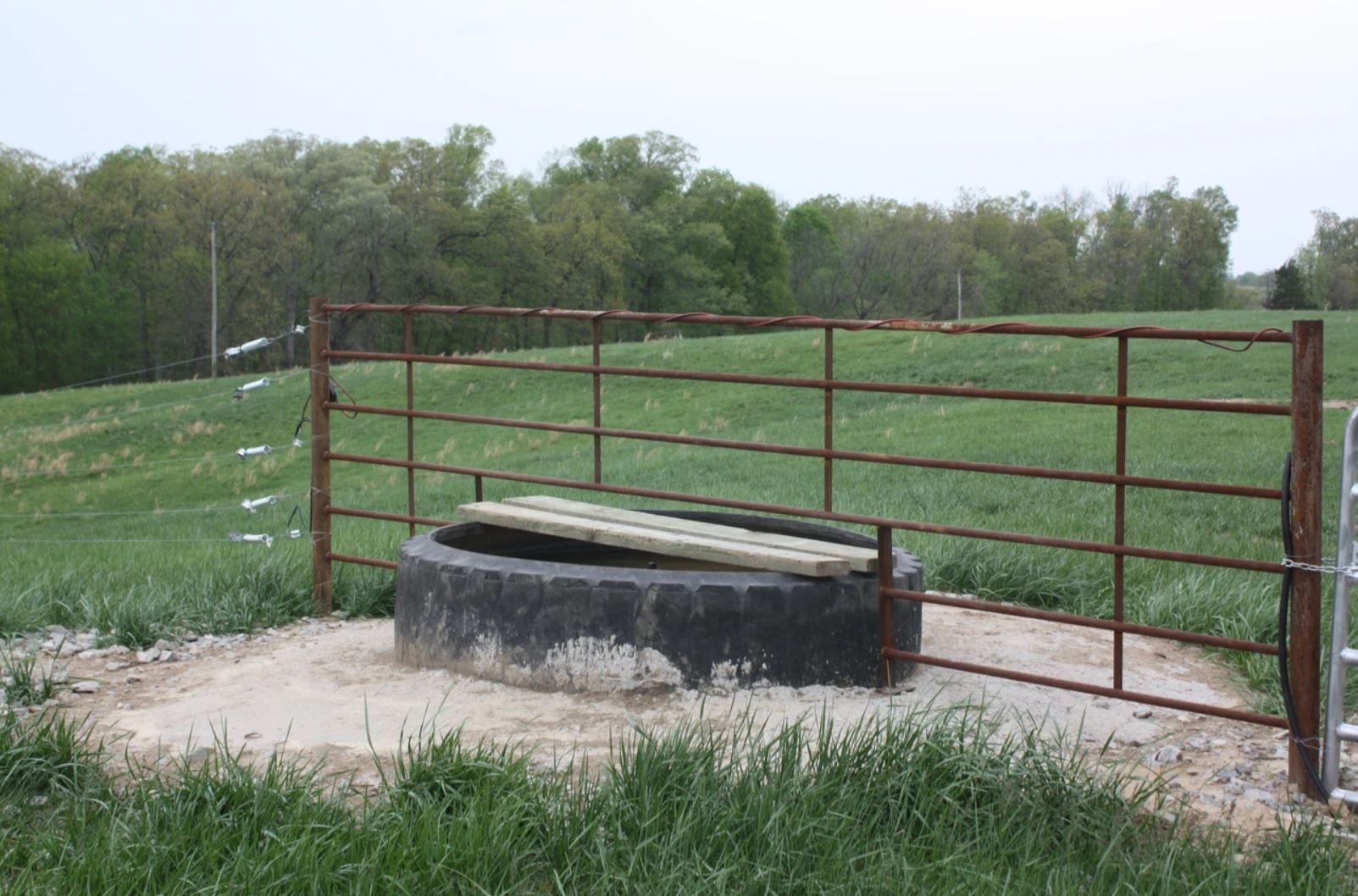 A fence surrounds a well in a grassy field
