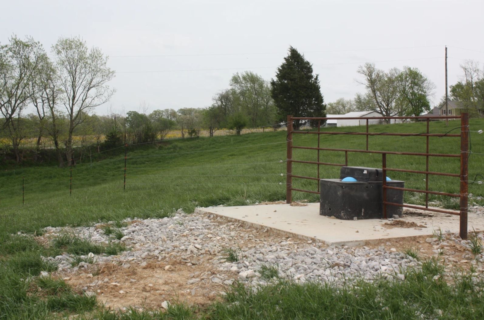 A fenced in area with a water tank in the middle of a grassy field.