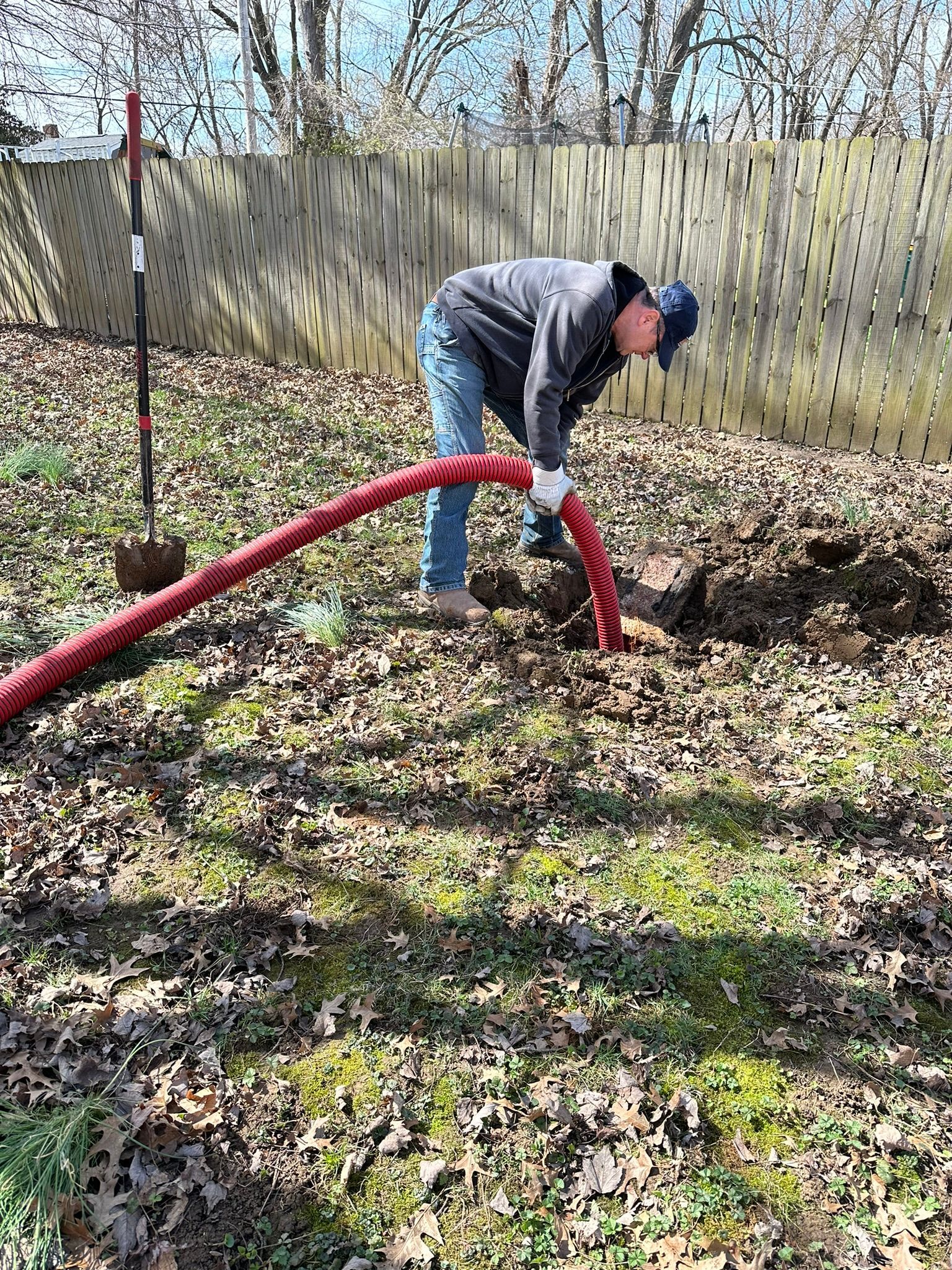 a man is using a red hose to dig a hole in the ground .