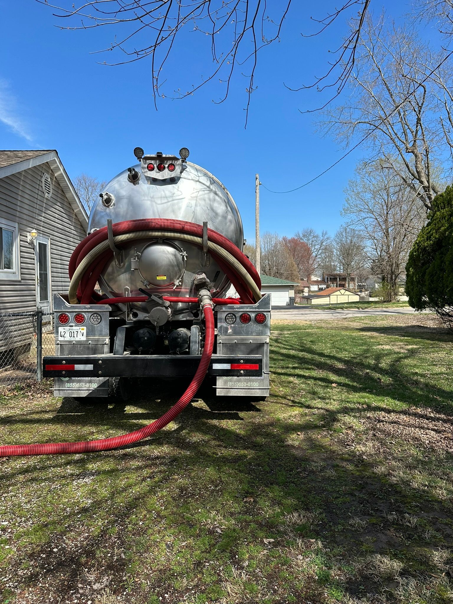 a vacuum truck is parked in front of a house with a red hose attached to it .