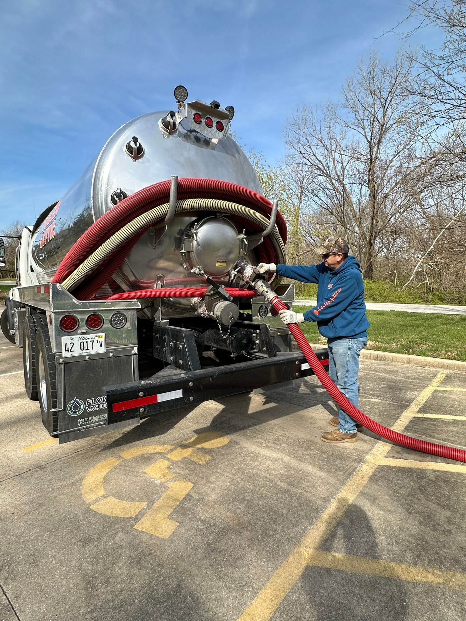 A man is attaching a hose to a vacuum truck in a parking lot.