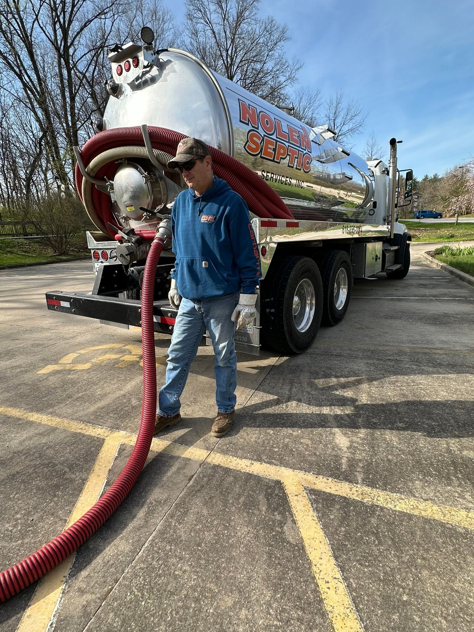 A man is standing next to a vacuum truck in a parking lot.