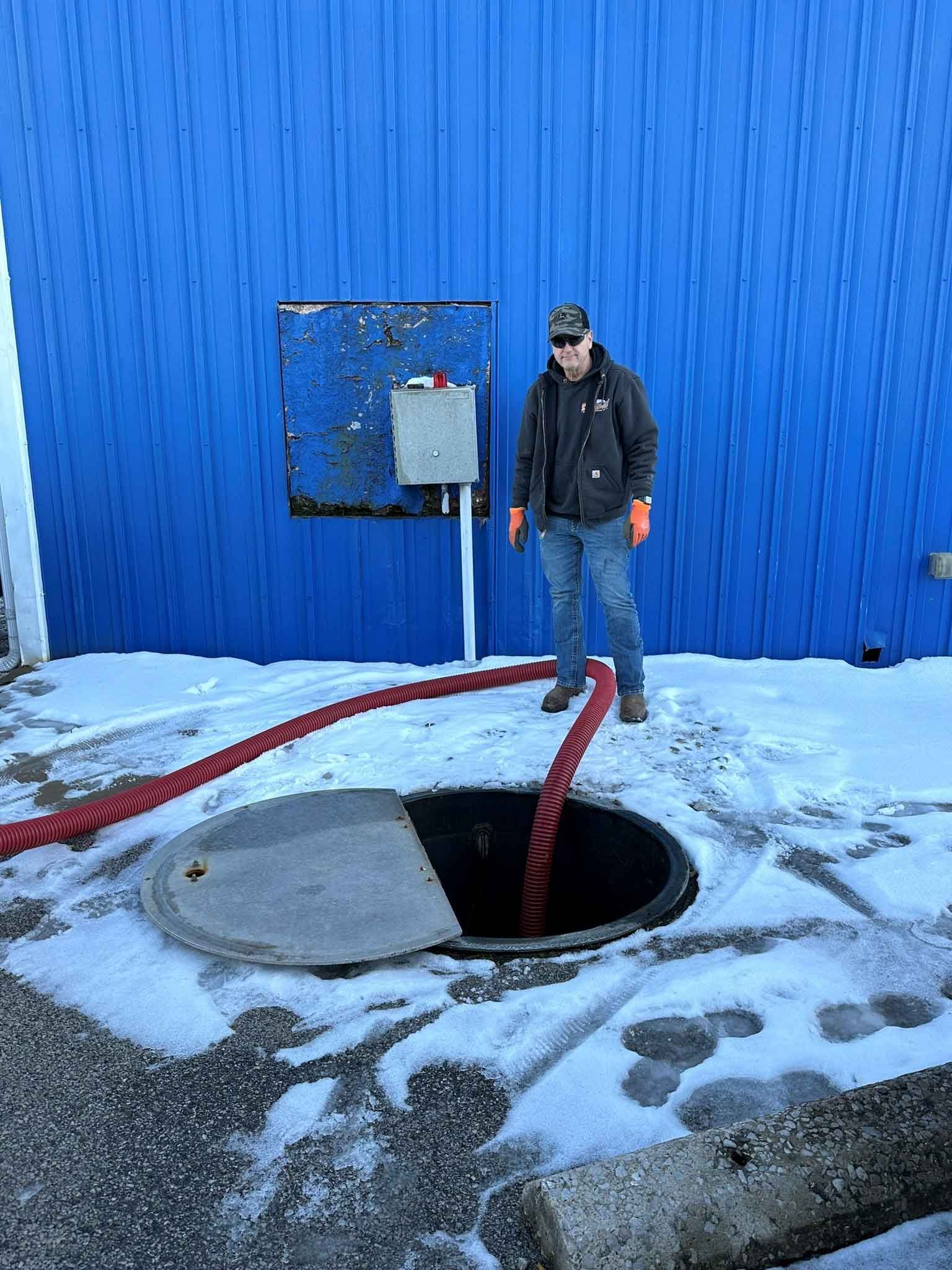 A man is standing next to a manhole cover in the snow.
