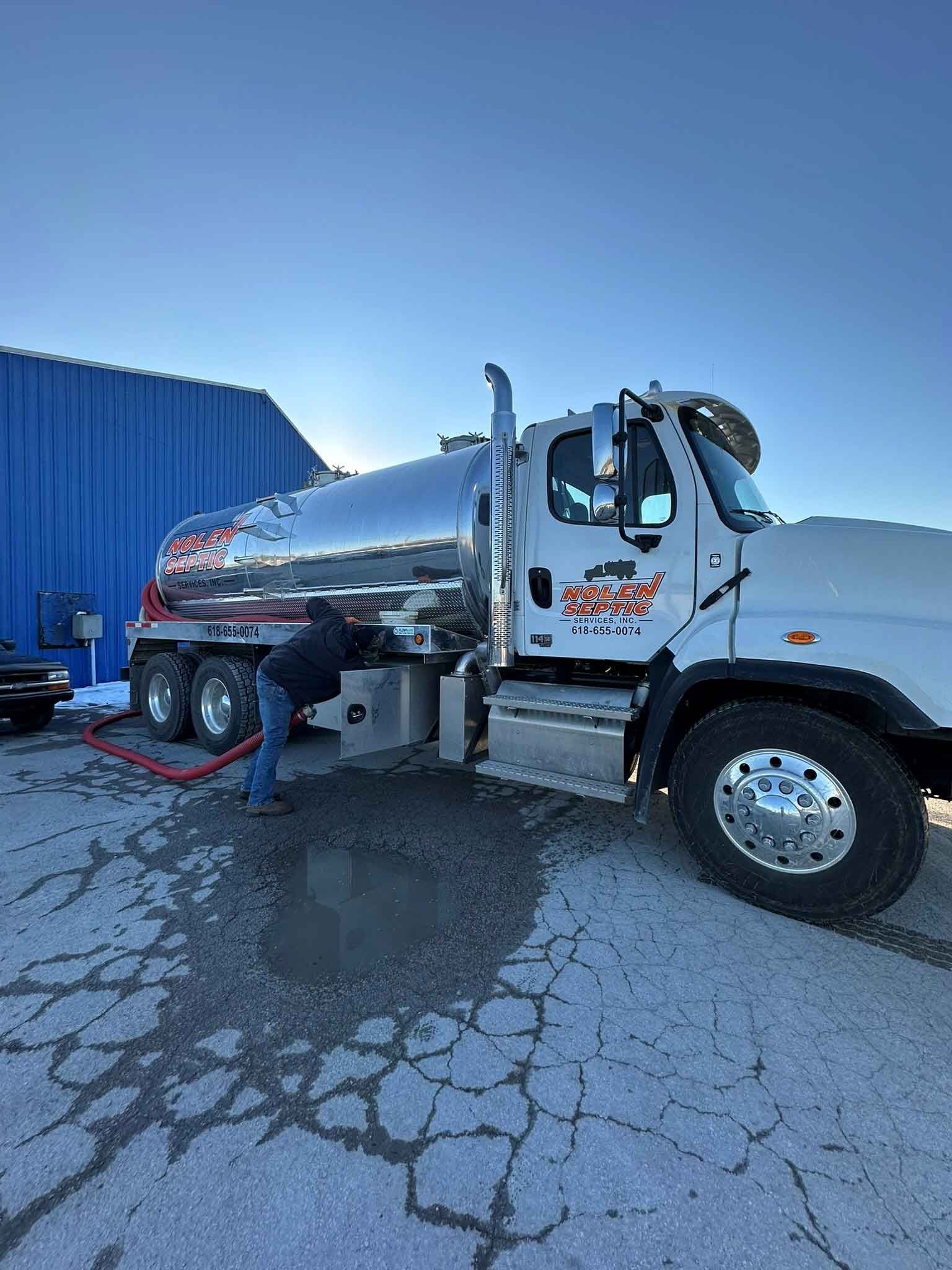 A man is working on a tanker truck in a parking lot.