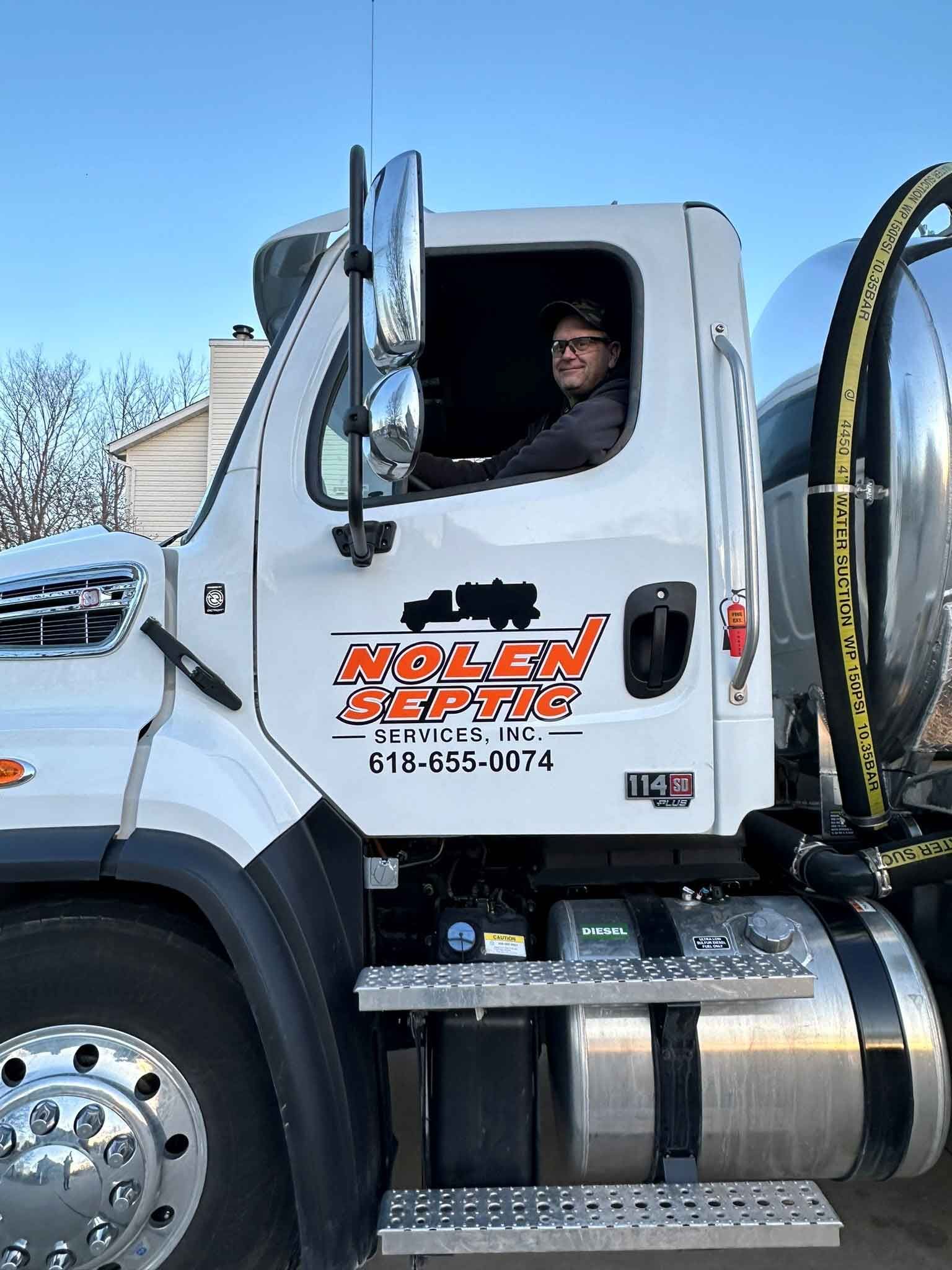 A man is sitting in the driver's seat of a vacuum truck.