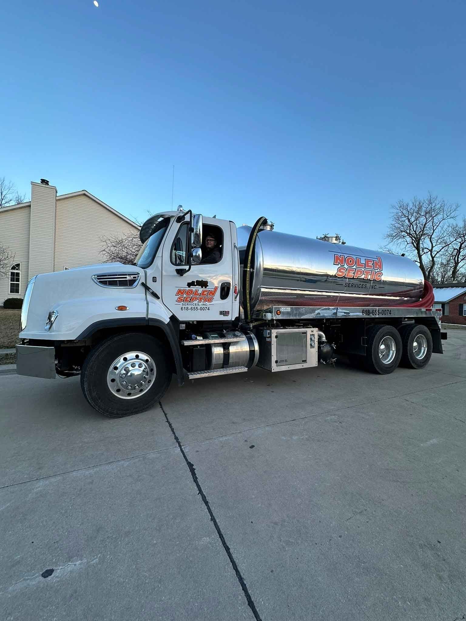 A large tanker truck is parked on the side of the road in front of a house.