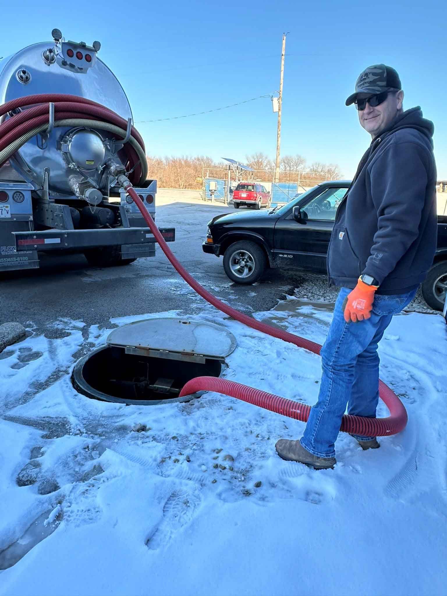 A man is standing in the snow next to a septic tank.