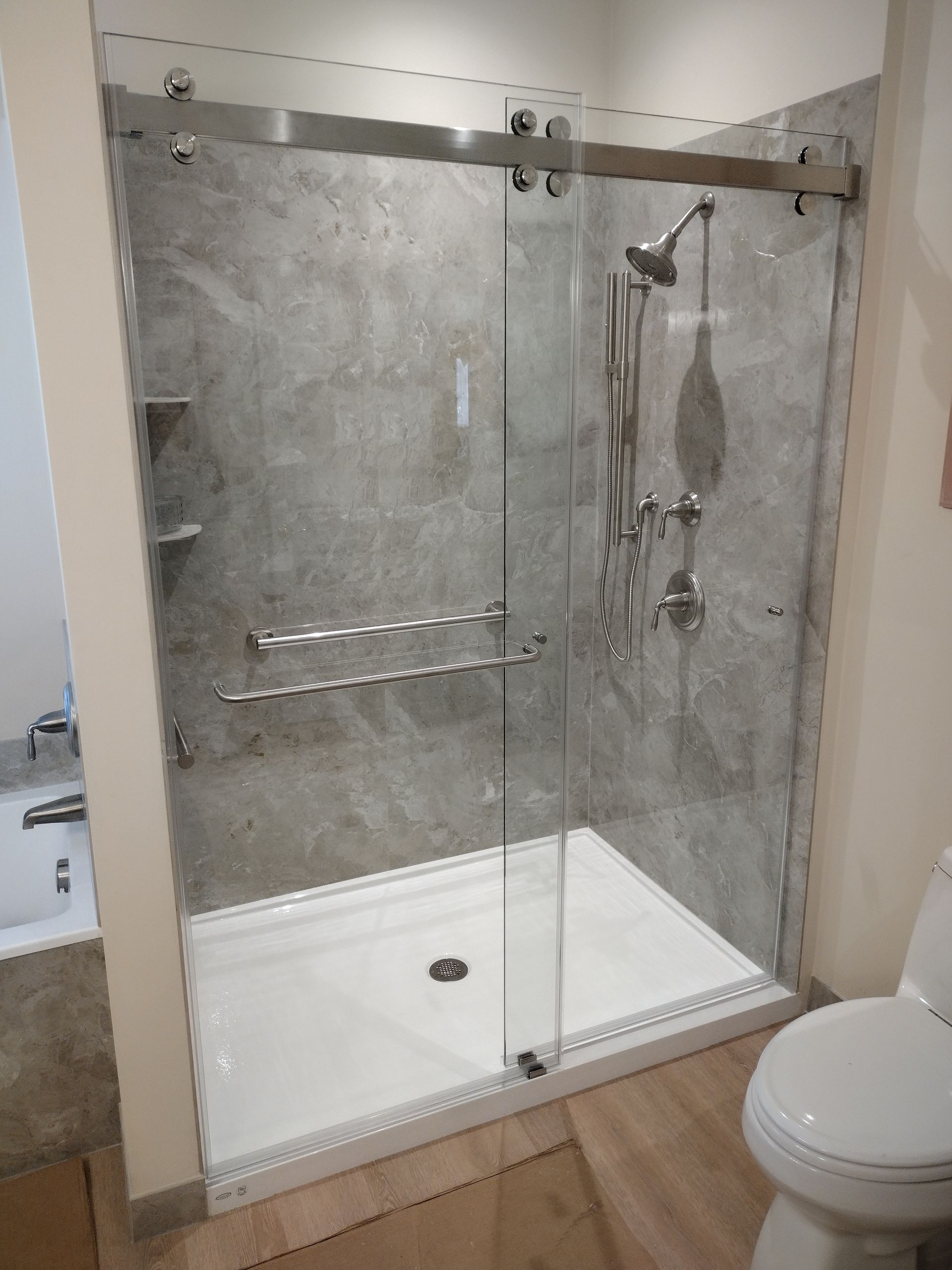 Modern walk-in shower with gray textured walls, glass door, and white base. Includes a toilet.