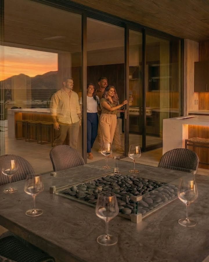 People standing on a balcony at sunset, looking out over a modern patio with a fire pit and wine glasses.