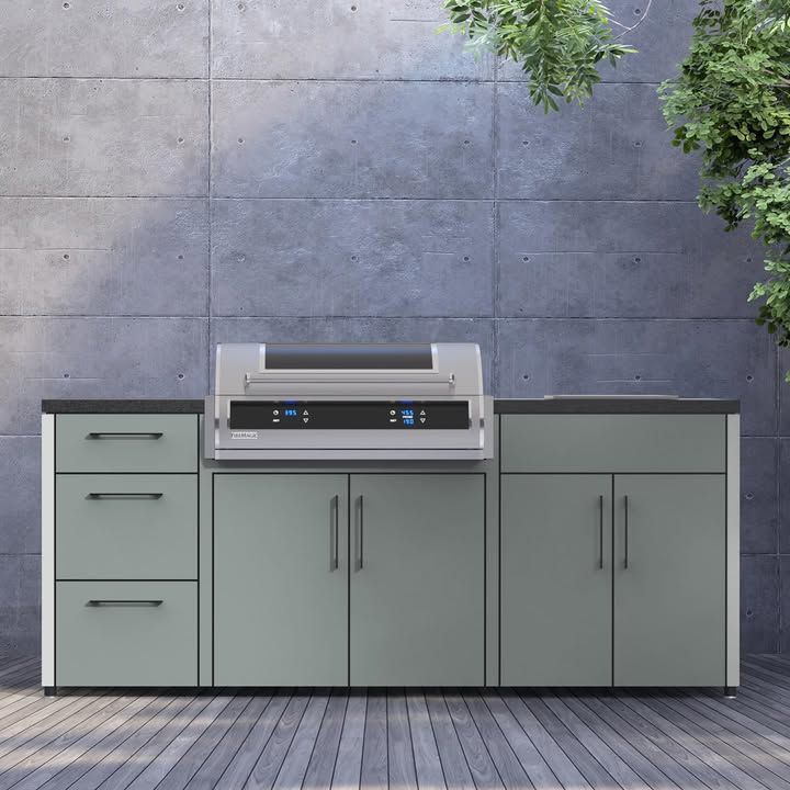 Modern outdoor kitchen with gray cabinets and built-in grill against a concrete wall.