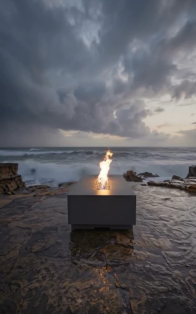 Fire burning in a metal fire pit on a rocky shore beneath dark storm clouds over the sea