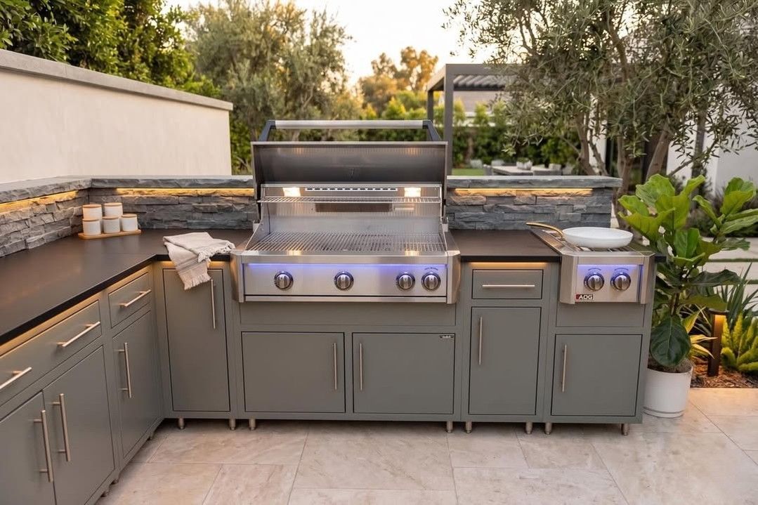 Outdoor gray built-in grill station with stainless steel barbecue, stone counters, and potted plants