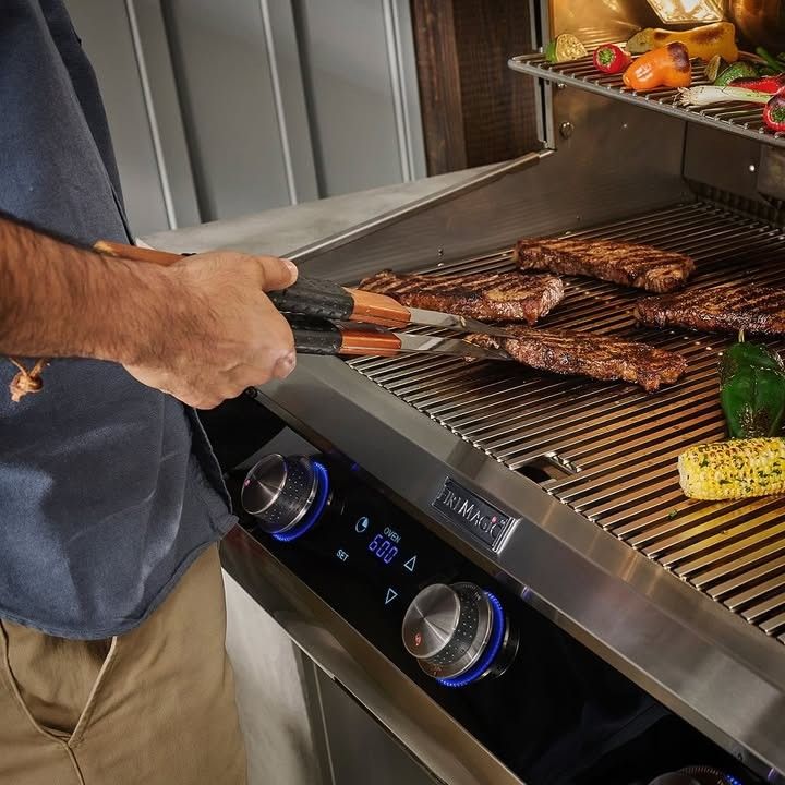 Person grilling meat and corn on a gas barbecue with metal tongs