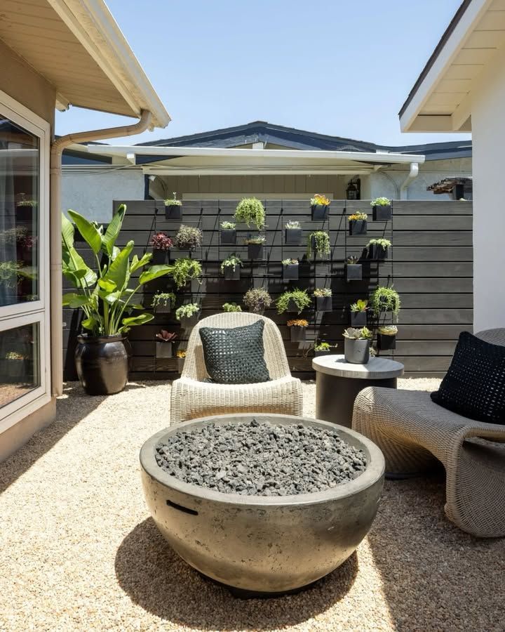 Small patio with white chairs, round fire pit, potted plants, and gray fence in bright sunlight