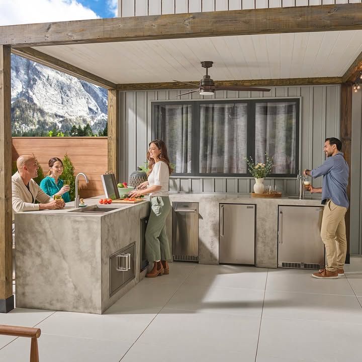 Modern outdoor kitchen with people socializing beside a mountain view and fire pit