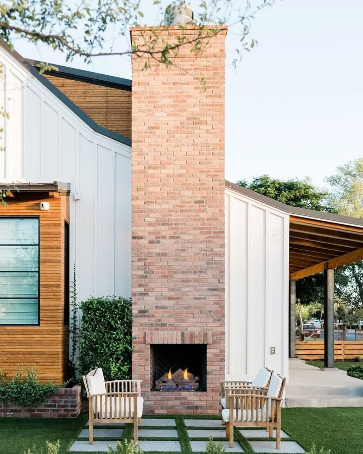 Modern house exterior with a tall brick fireplace, white siding, and two chairs on a green lawn