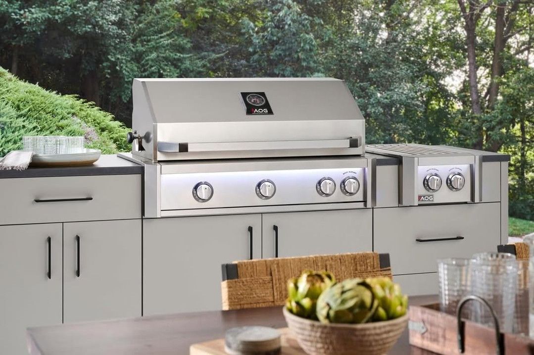 Outdoor stainless steel grill station with white cabinets and a table of bowls and glasses in front