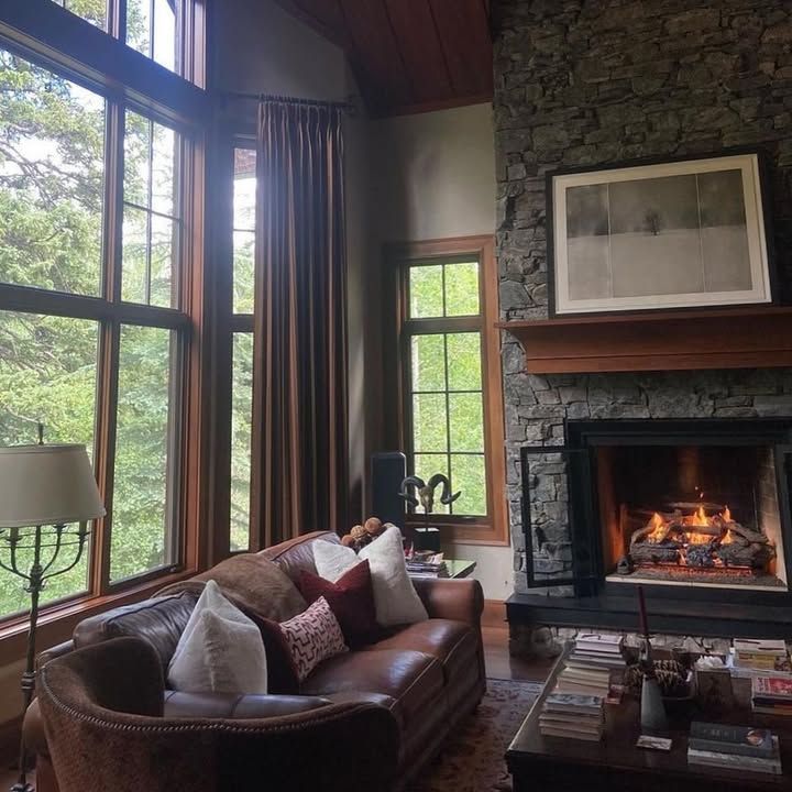 Cozy living room with leather sofa, large windows, stone fireplace, and a lit fire