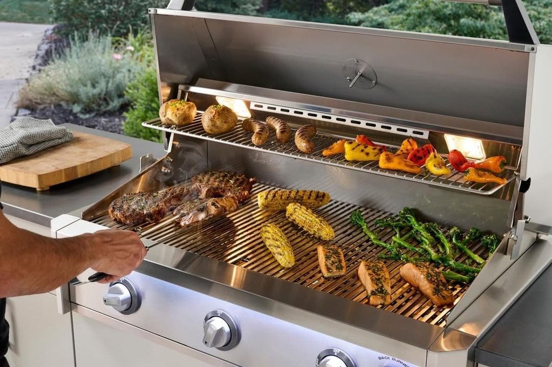 Hands grilling assorted meats and vegetables on a stainless steel barbecue.