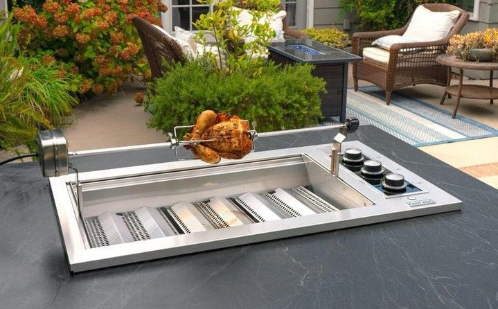 Outdoor stainless steel grill cooking a roasted chicken on a patio, with lounge chairs and plants nearby