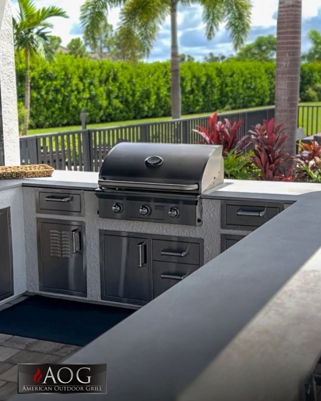 Outdoor stainless steel grill and cabinet kitchen on a patio with tropical landscaping