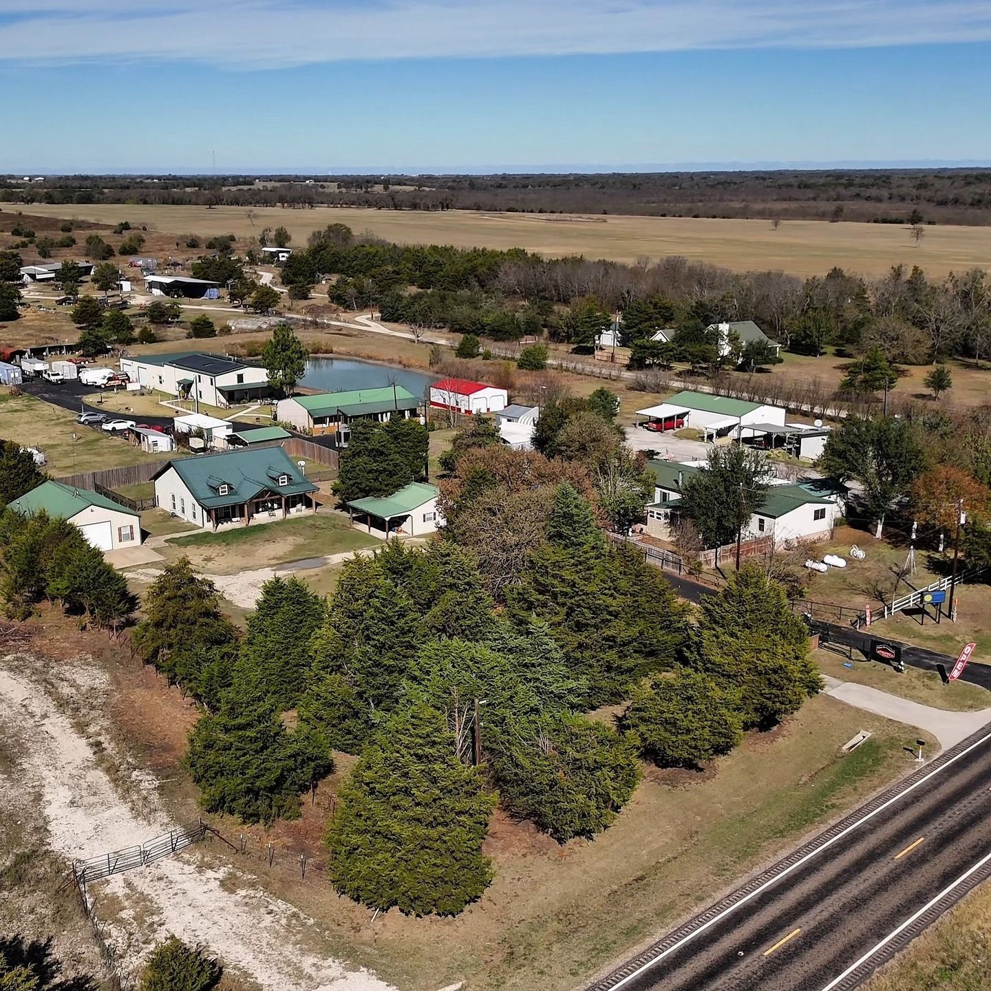 Aerial view of a rural campground with cabins, trees, dirt roads, and a railroad track beside open fields.