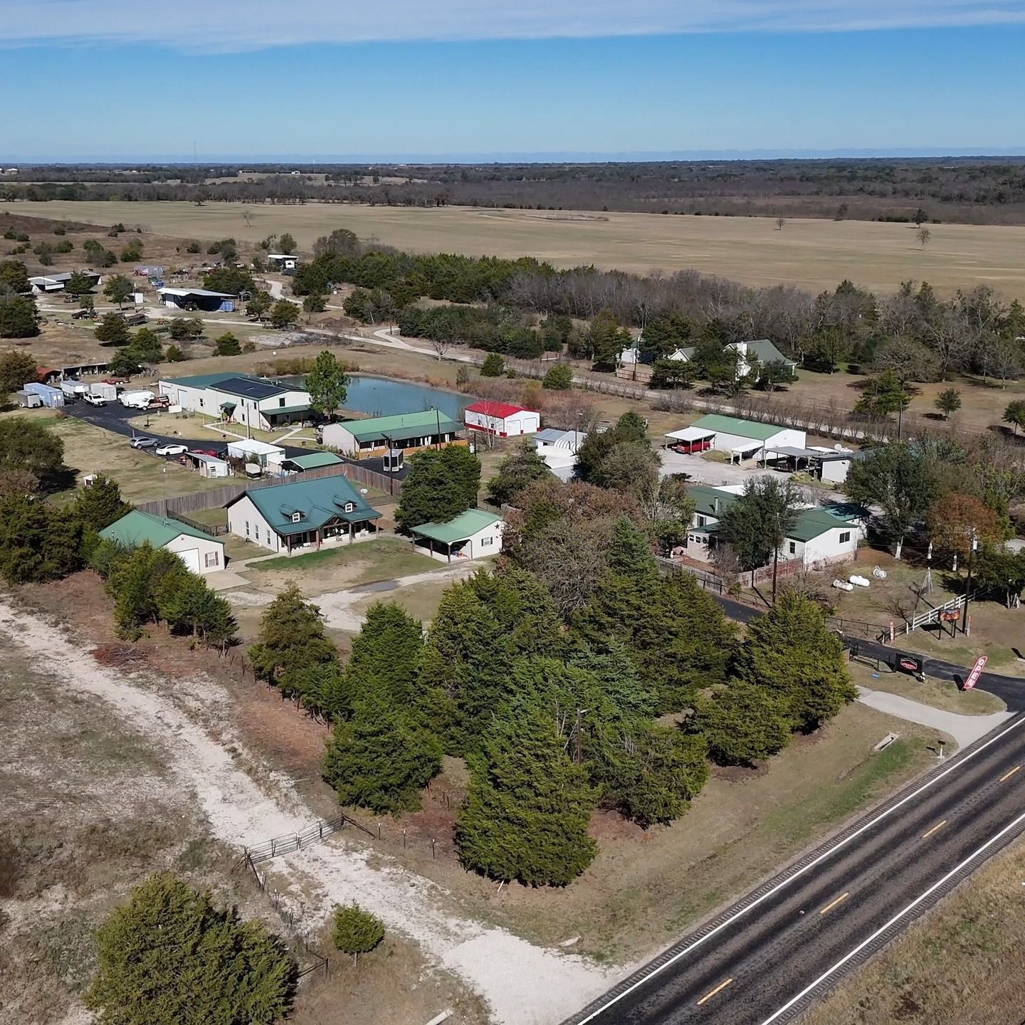 Aerial view of a small rural settlement with houses, trees, and roads beside open fields
