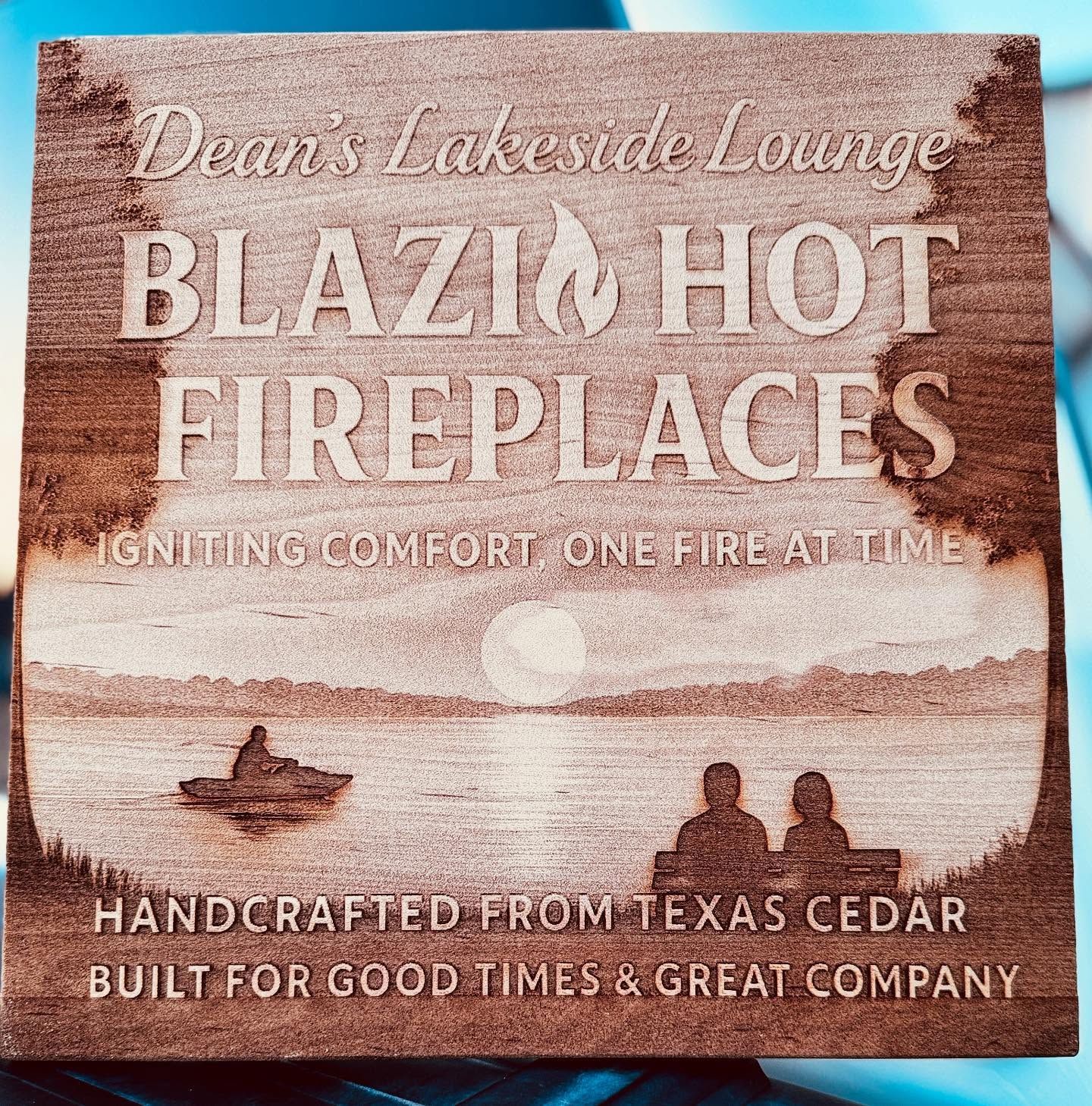 Sign for Blazing Hot Fireplaces with a lakeside sunset and people in boats; handcrafted from Texas cedar.