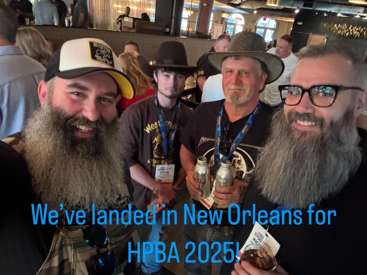 Three bearded men in hats pose indoors at a New Orleans bar; text says “We’ve landed in New Orleans for HPBA 2025”
