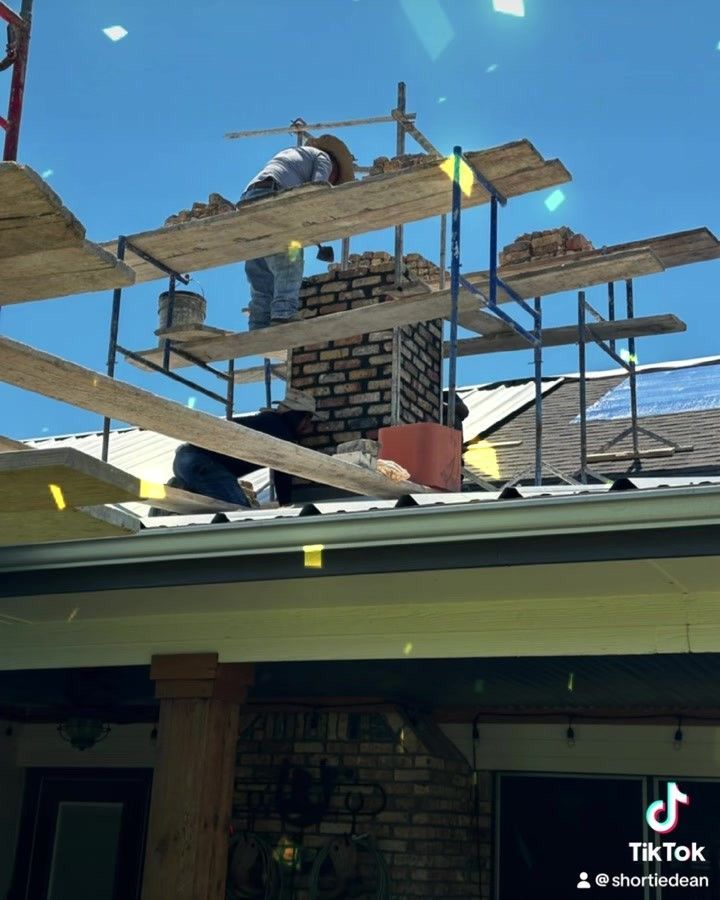 Workers repairing a brick chimney on a house roof under a bright blue sky