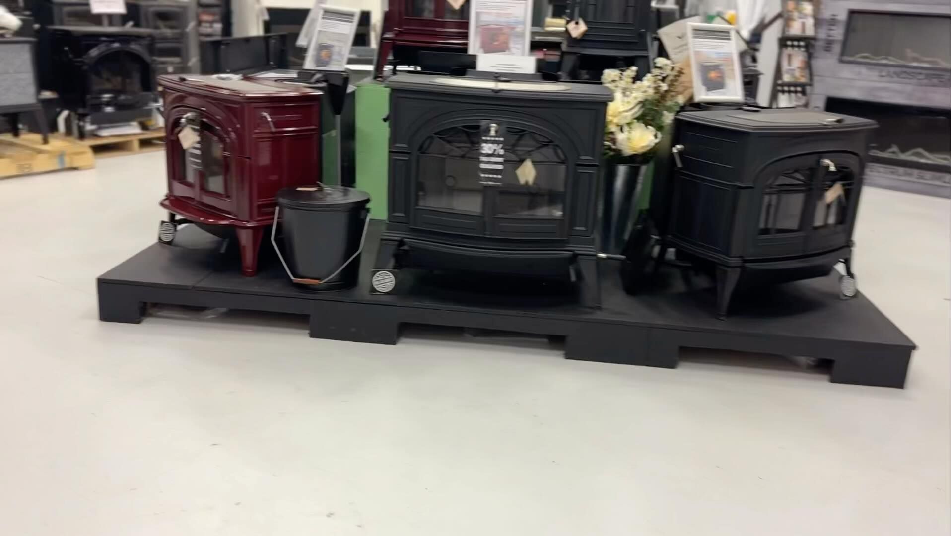 Three decorative electric fireplaces on a black display platform in a store aisle, in red, green, and black.