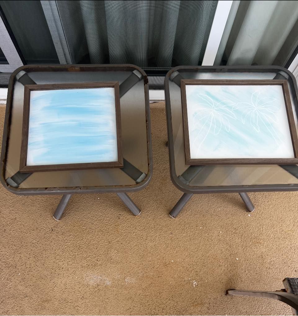 Two small square side tables with frosted glass tops on a patio beside a corrugated metal wall.