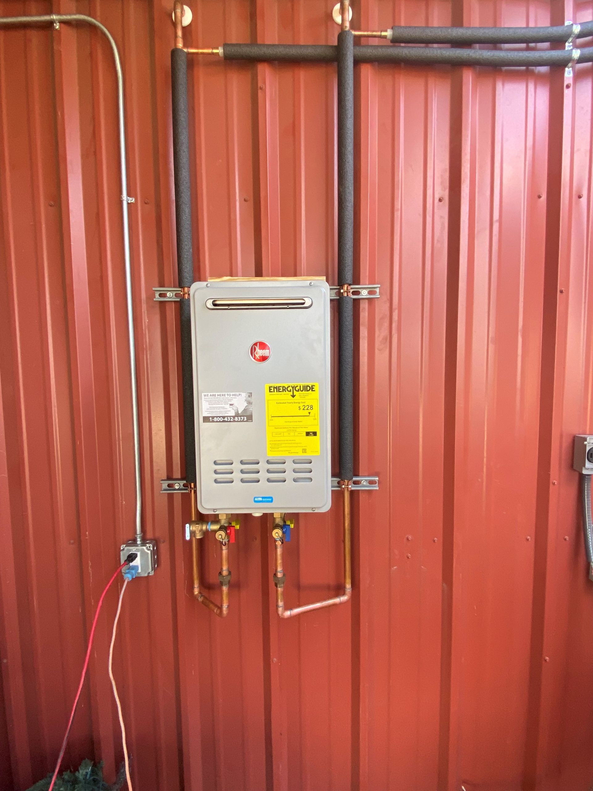 A water heater is hanging on a red metal wall.