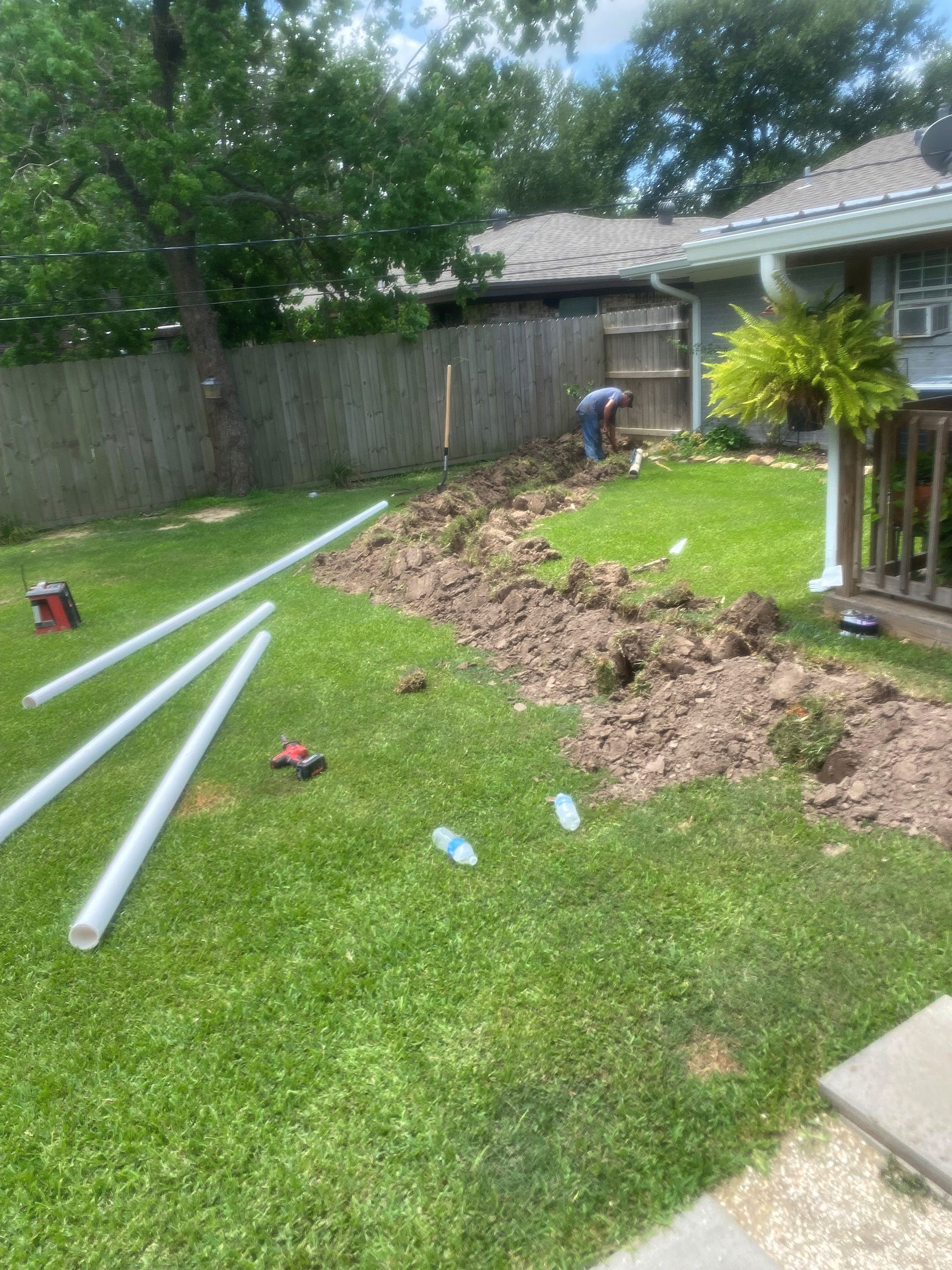 A man is working on a drainage system in a backyard.