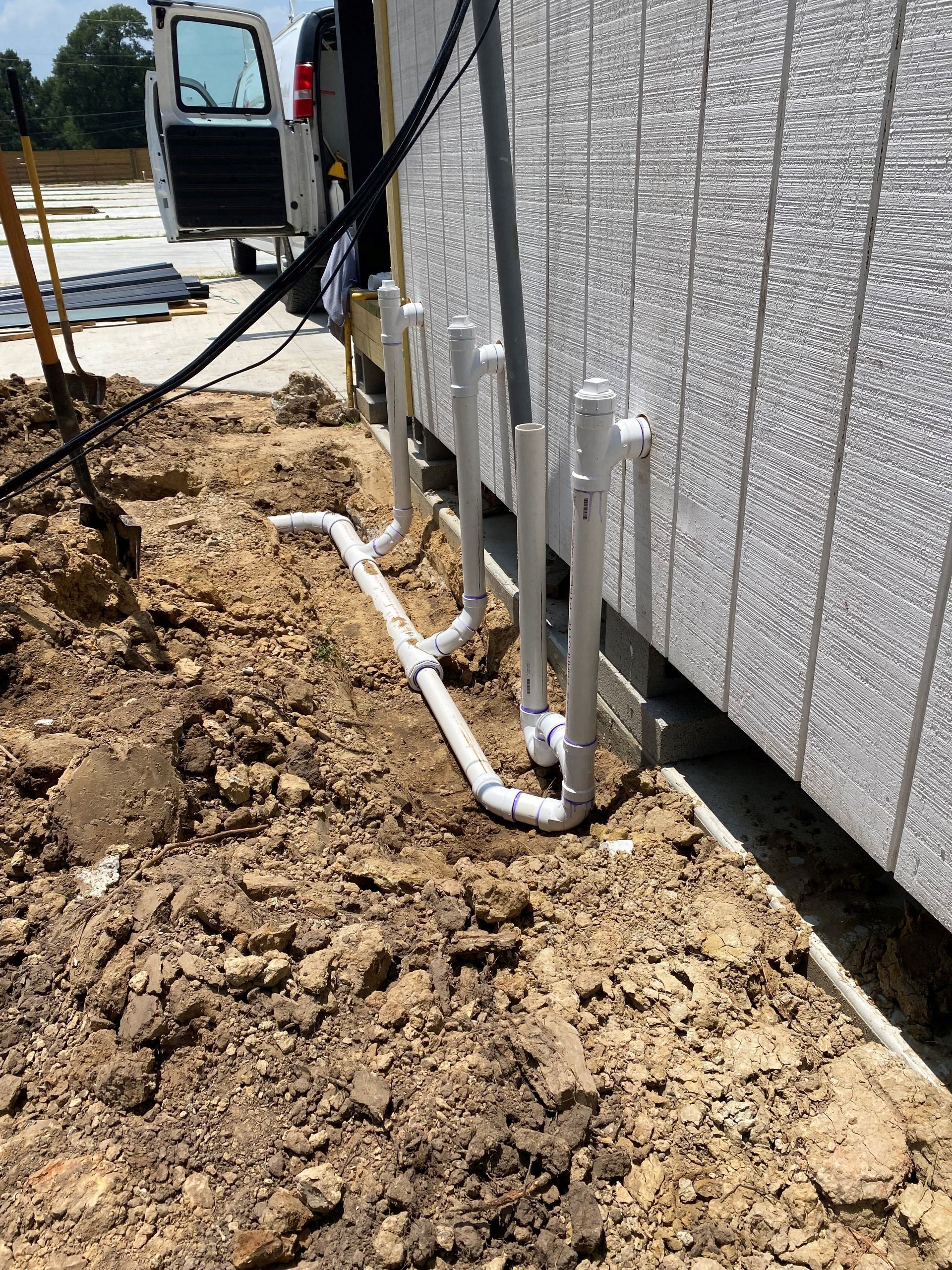 A white van is parked in the dirt next to a building.