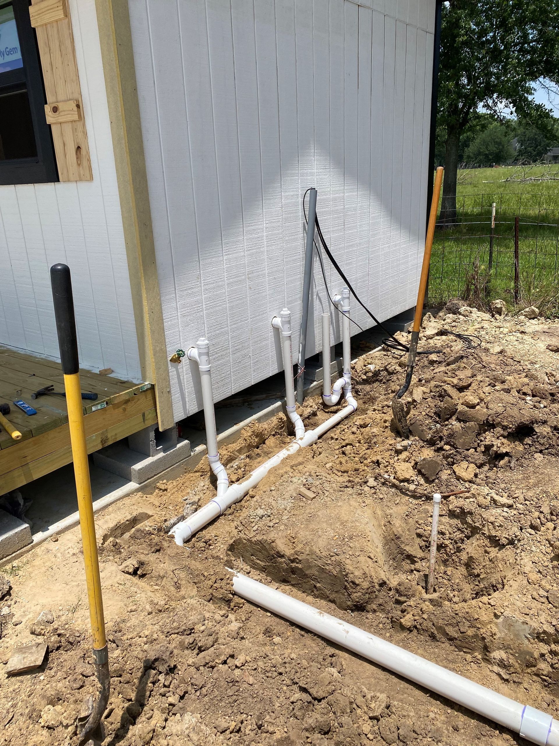 A bunch of pipes are laying in the dirt in front of a house.