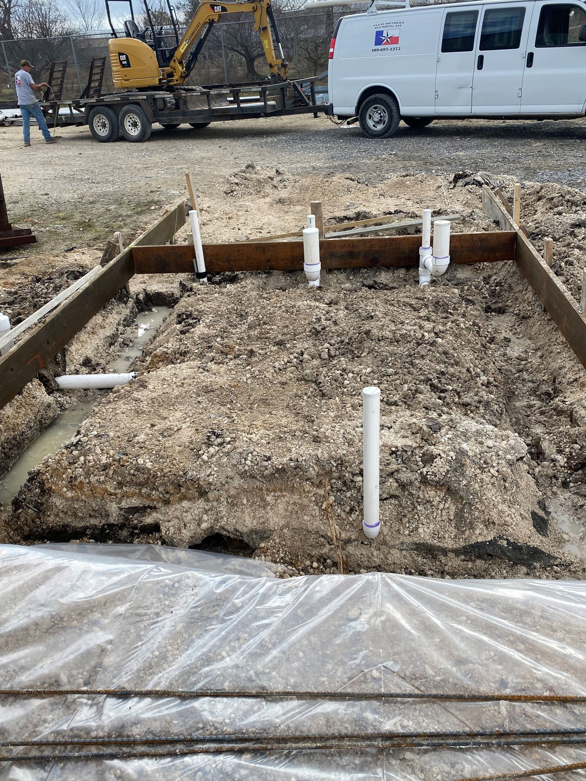A white van is parked in a dirt lot next to a construction site.